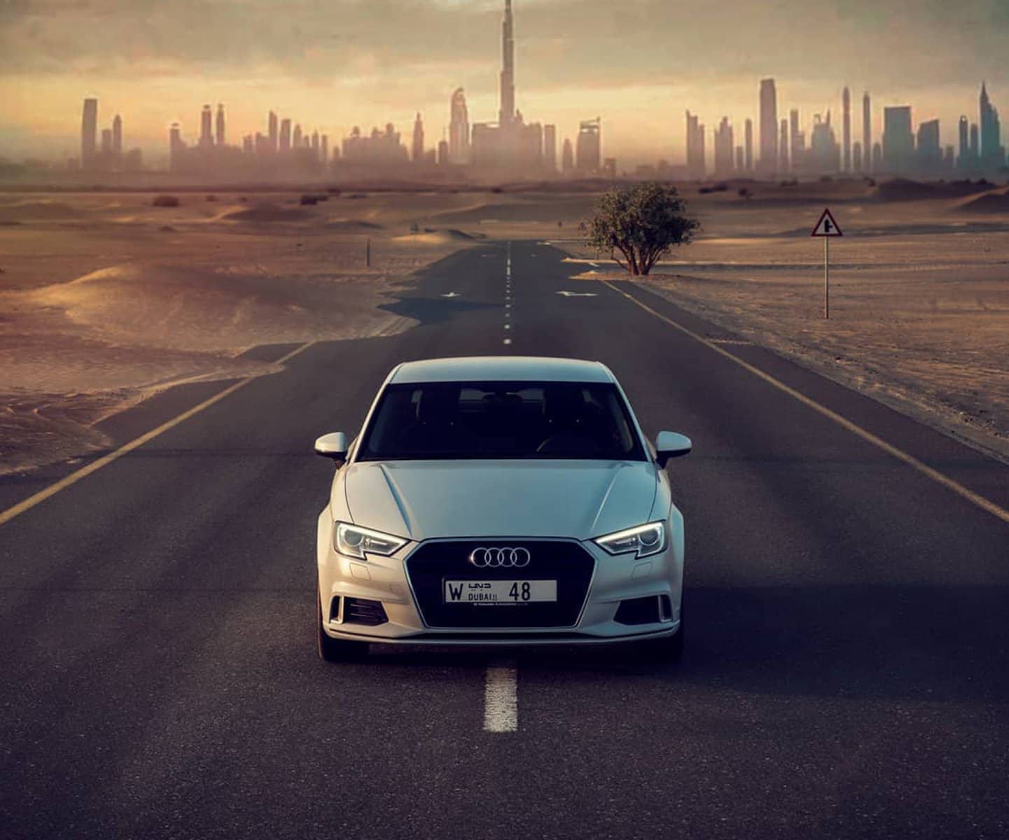 White Audi on a desert road with the Dubai skyline behind