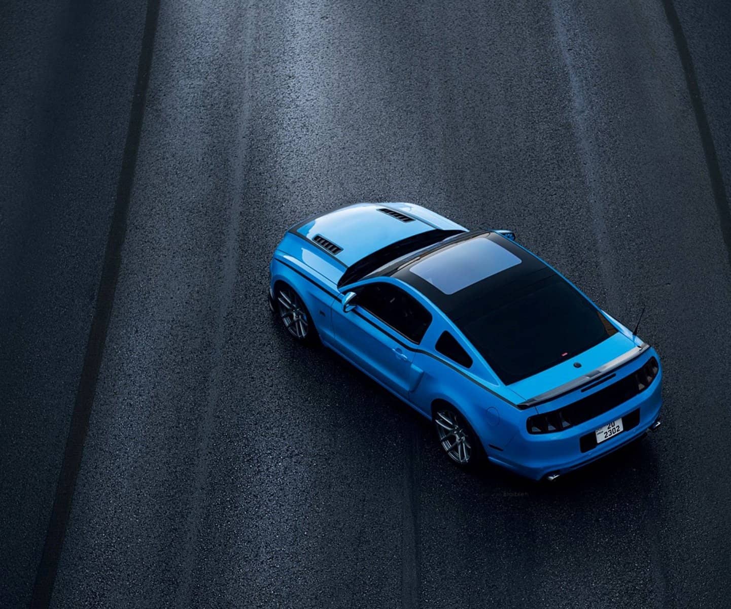 Blue Mustang from above on dark asphalt
