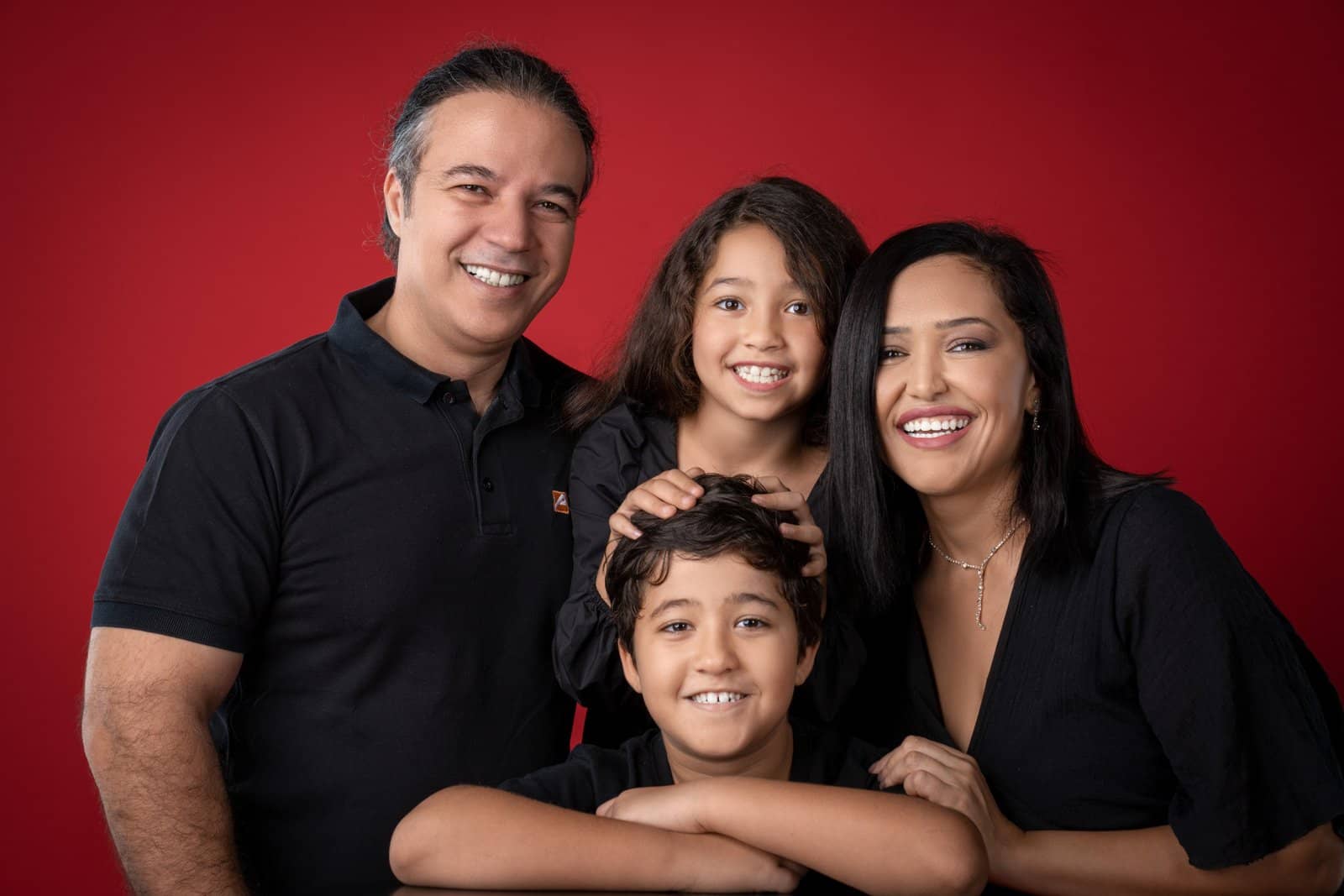 Family of four smiling together against a red backdrop