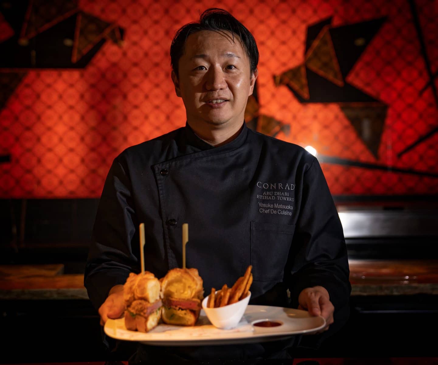 Chef presenting a plate against a red wall