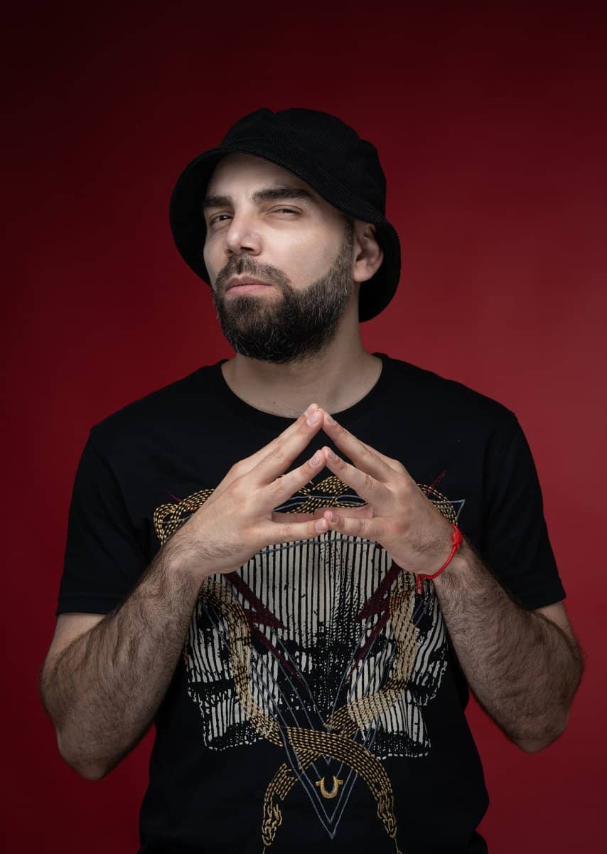 Man in a bucket hat with steepled hands on red
