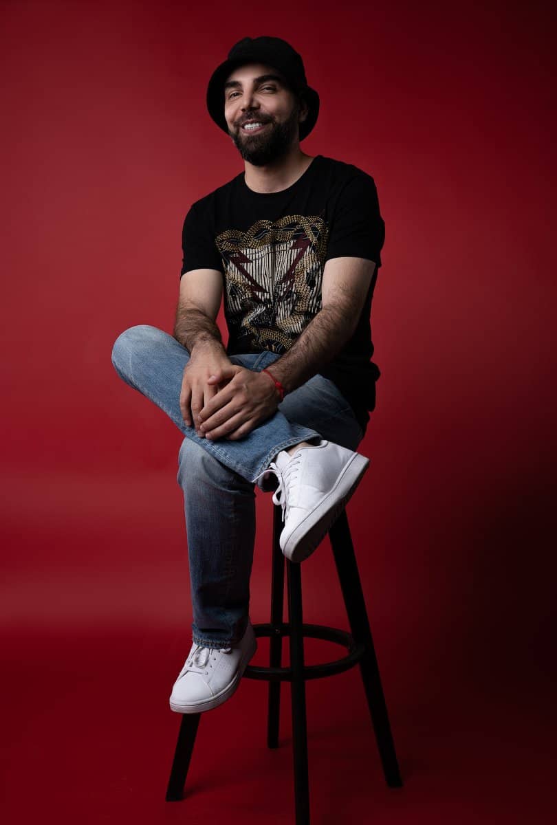 Man seated on a stool against a red backdrop