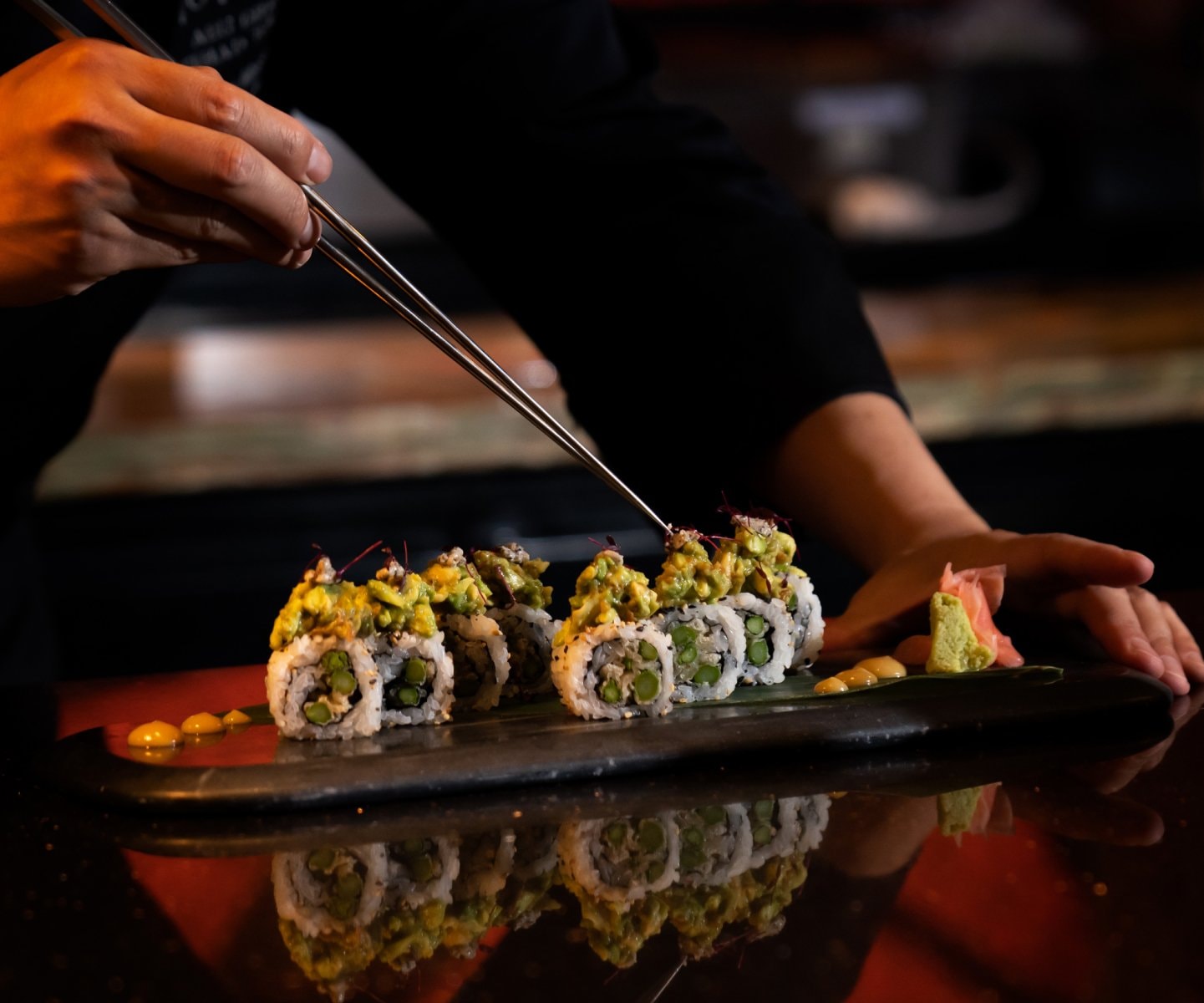 Sushi rolls lifted with chopsticks on a dark counter