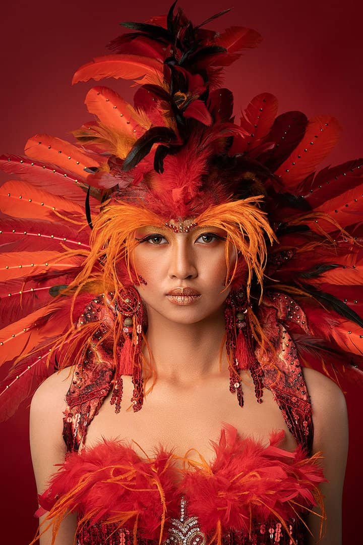 Model in a crimson feathered headdress under red studio light