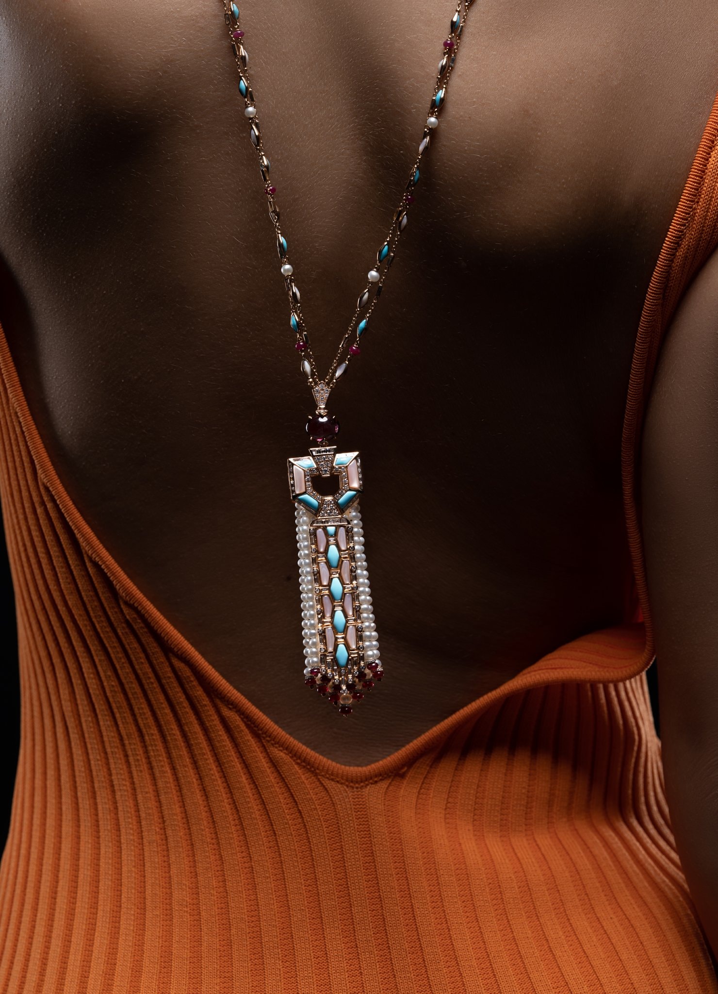 Gold pendant necklace resting on skin against a bronze knit